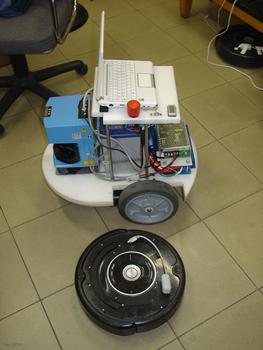 Robot líder, con sensor láser, junto a un robot de limpieza convencional, de tamaño inferior.
